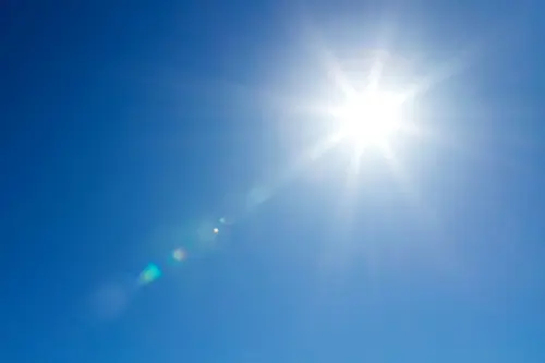 Strahlende Sonne am wolkenlosen, blauen Himmel, deren Strahlen in der Luft Lichtreflexionen erzeugen.