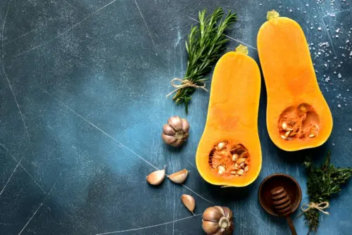 Zu sehen ist ein aufgeschnittener Butternut-Kürbis, um den Knoblauch und andere Gewürze angerichtet sind.