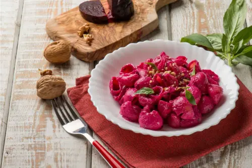 Pink Pasta mit Walnuessen und Basilikum auf einem weissen Teller neben ganzen Walnusskernen.[Foto: AdobeStock_Marco Mayer]