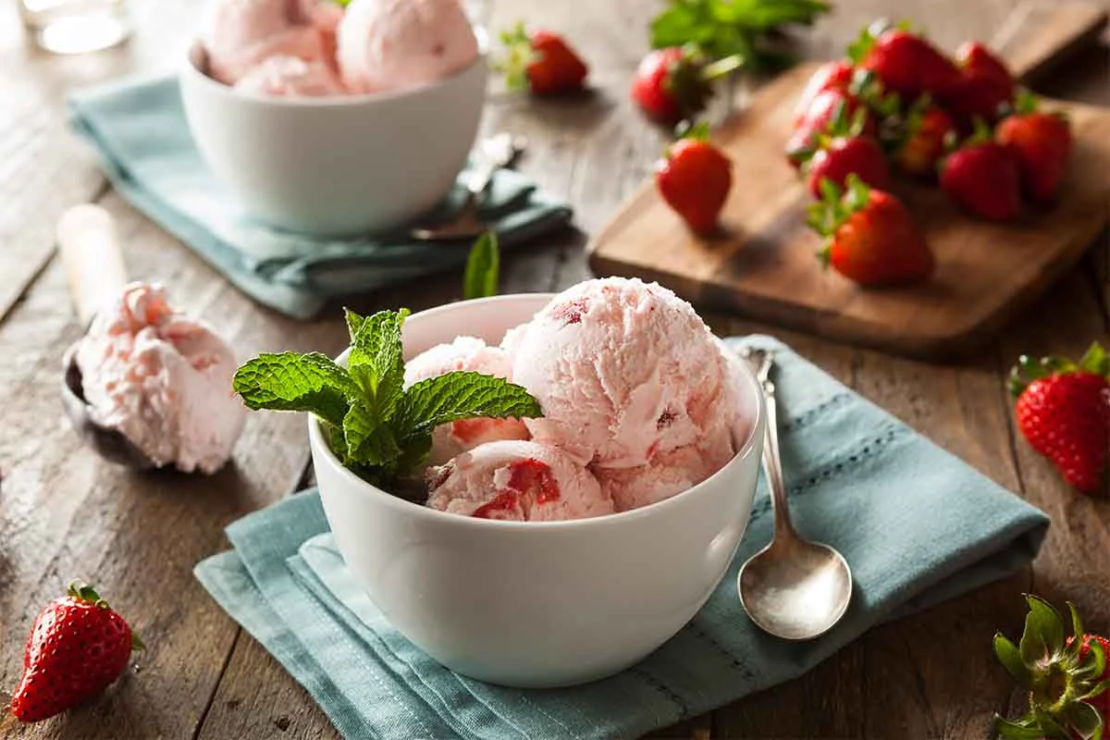 Frozen Joghurt Rezept in einer Schale mit Minze und daneben ein paar Erdbeeren [Foto: AdobeStock_Brent Hofacker]