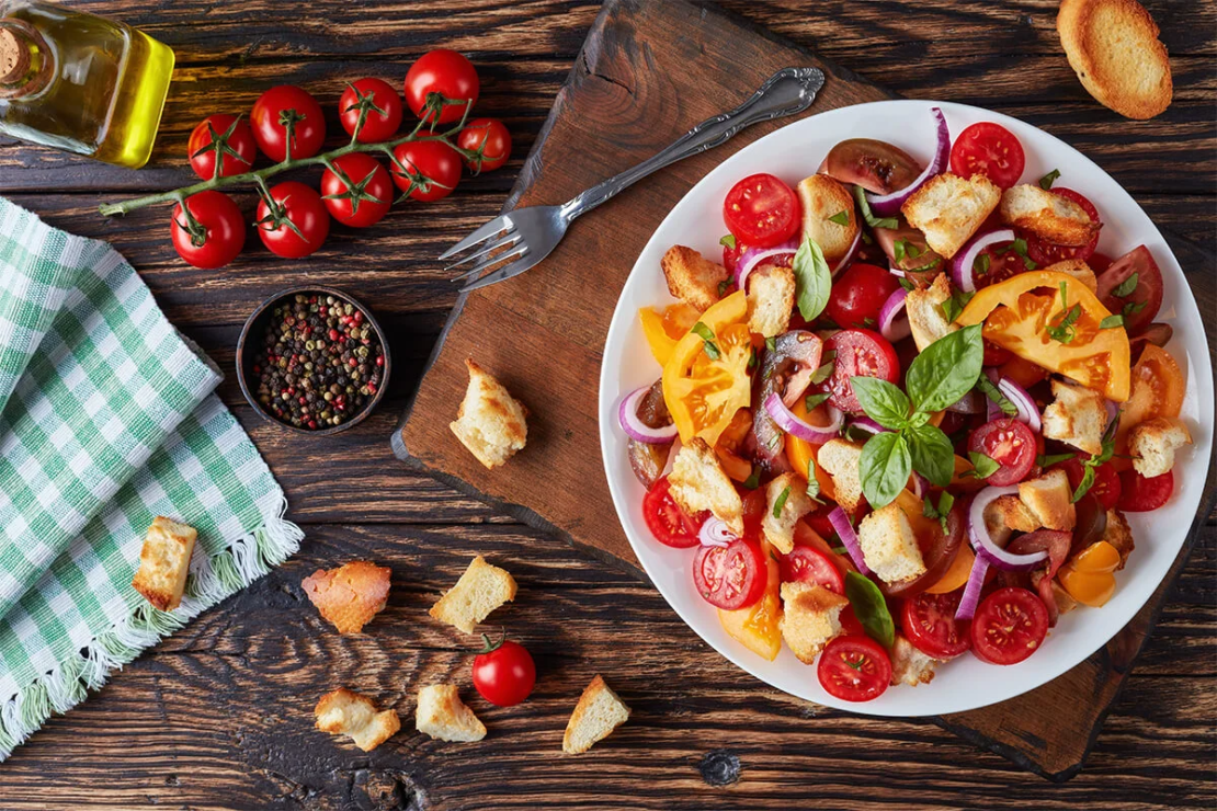 Angerichteter Tomatensalat mit gerösteten Brotwürfeln und Basilikum auf einem Holztisch