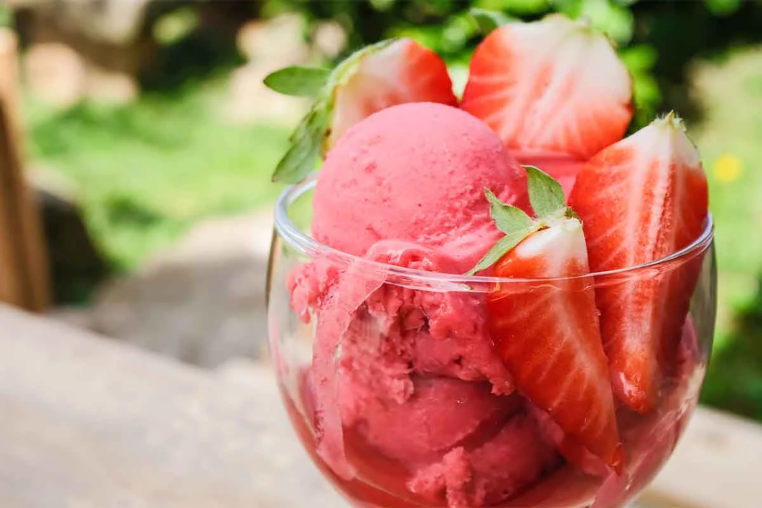 Erdbeereis ohne Eismaschine gemacht und serviert in einem Eisbecher aus Glas – im Hintergrund eine Gartenkulisse [Foto: AdobeStock_S-Motive]