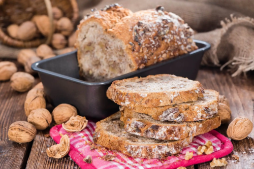 Walnussbrot liegt geschnitten auf einem Holztisch neben Walnüssen [Foto: AdobeStock_HandmadePictures]