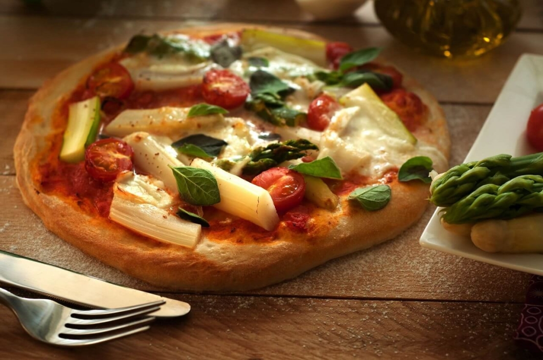 Spargelpizza mit Tomaten auf Holztisch