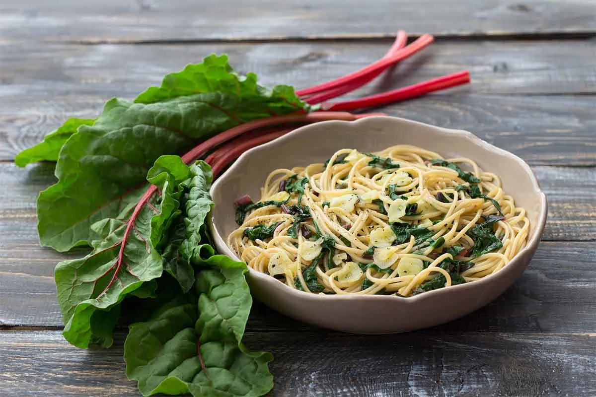 Mangoldpasta neben Stielen und Blaettern auf einem Tisch aus rustikalem Holz [Foto: AdobeStock_Olepeshkina]