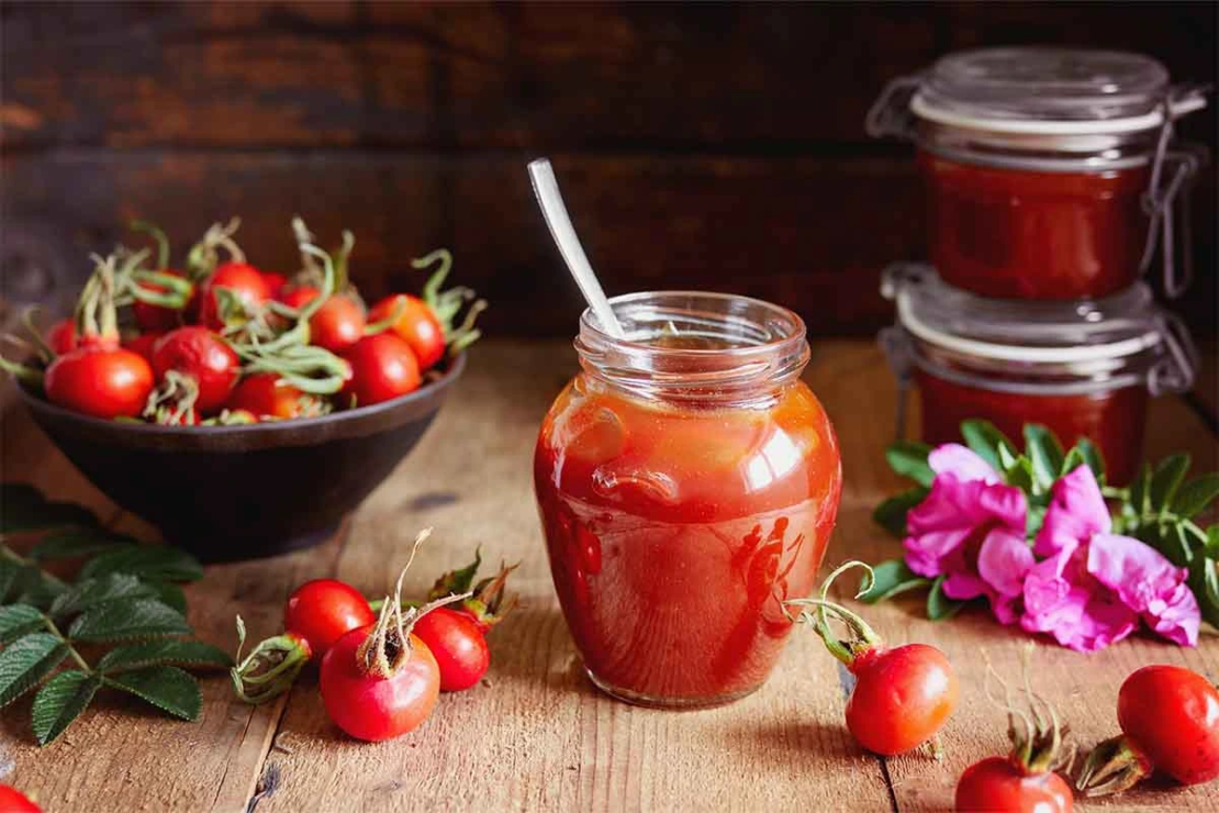 Glas mit Hagebutten-Marmelade neben frischen Hagebutten [Foto: AdobeStock_Melica]