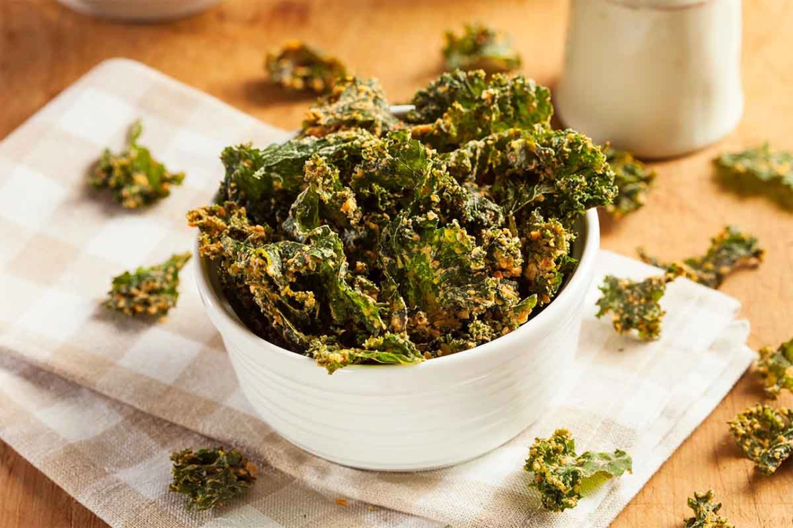 Kale Chips mit Gewürzen in einer kleinen weißen Schale, die auf einem Geschirrtuch steht. [Foto: AdobeStock_Brent Hofacker]