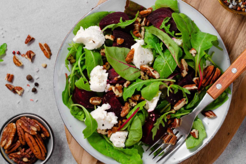 Rote-Bete-Salat mit Pfluecksalat, Pekanuessen und Feta von oben fotografiert. Auf dem Keramikteller liegt eine Gabel. [Foto: AdobeStock_julie208]